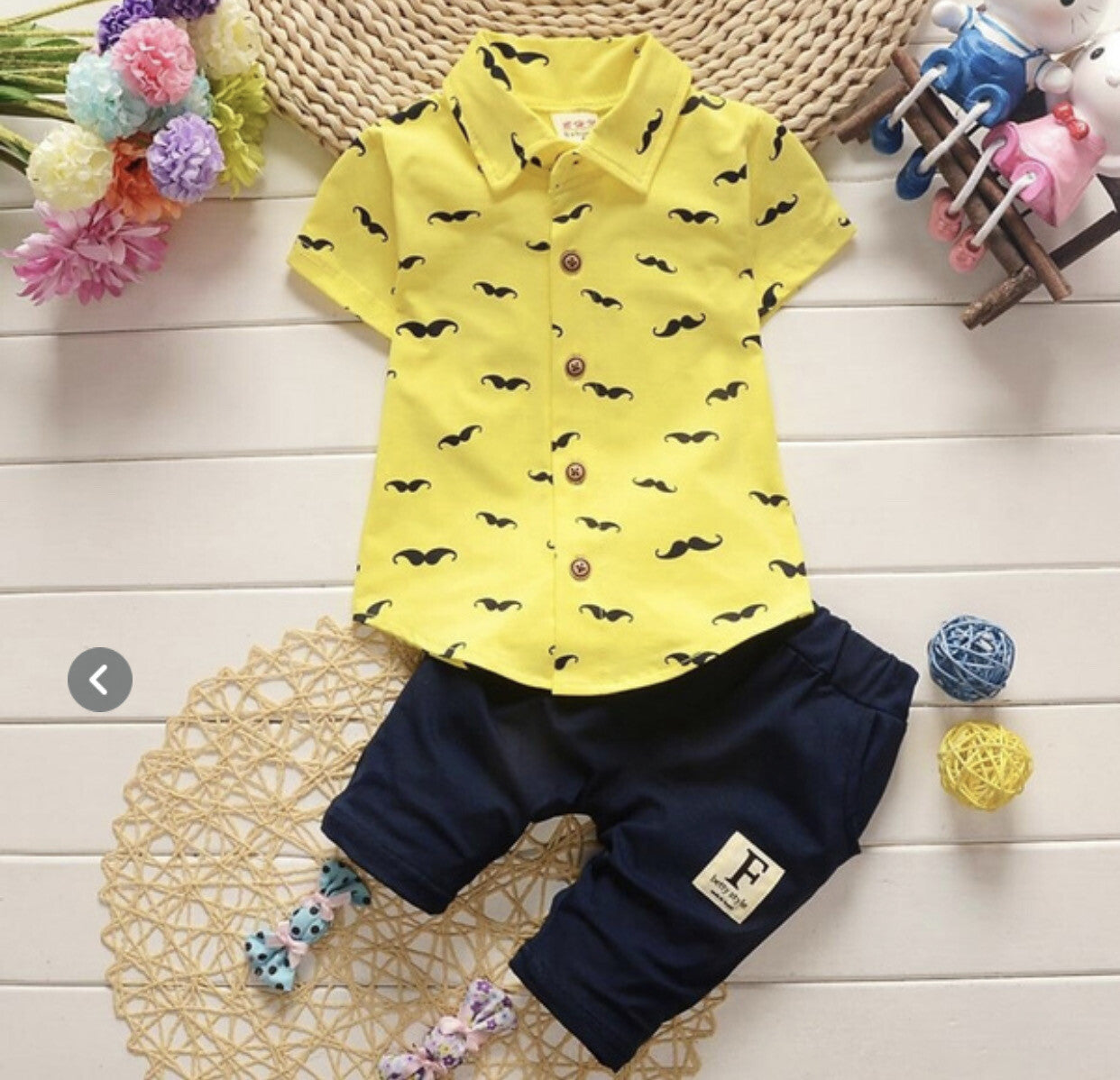 Yellow shirt with black mustache pattern and navy pants on a wooden surface with decorative items.