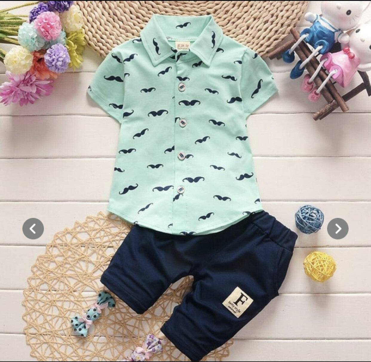 Children's outfit with mint green shirt and navy pants on a wooden surface with decorative elements.