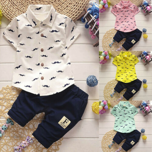 Children's clothing set with mustache pattern shirt and navy pants on a wooden surface.