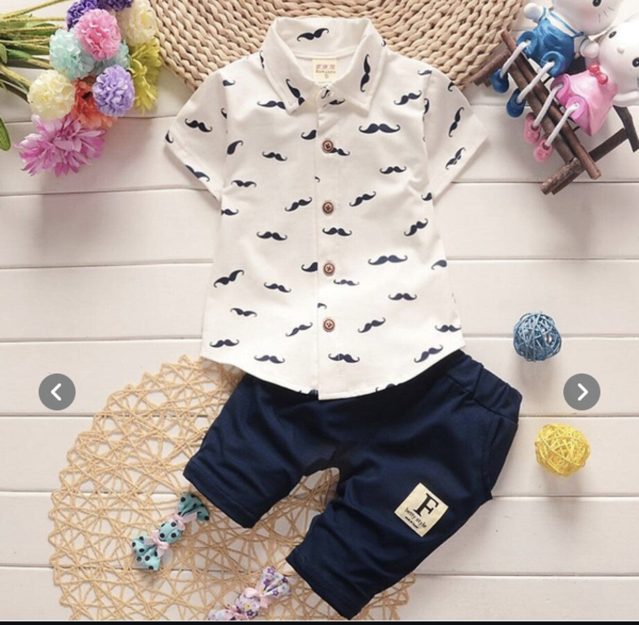 Children's outfit with white shirt and navy pants on a wooden surface with decorative elements.