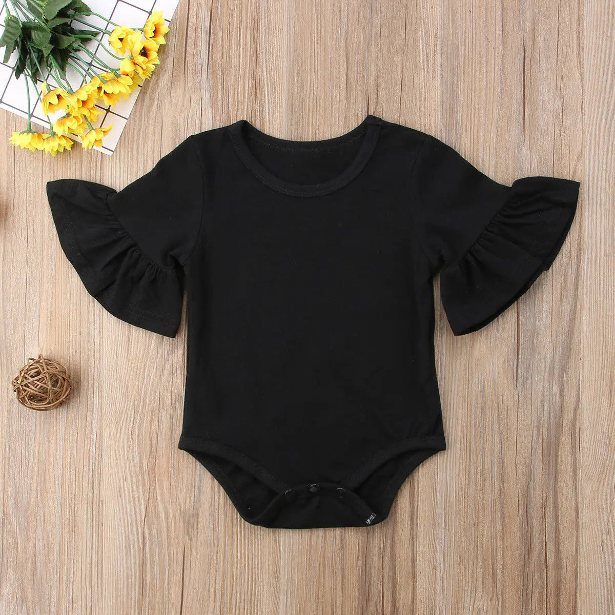 Black baby romper with ruffled sleeves on a wooden surface