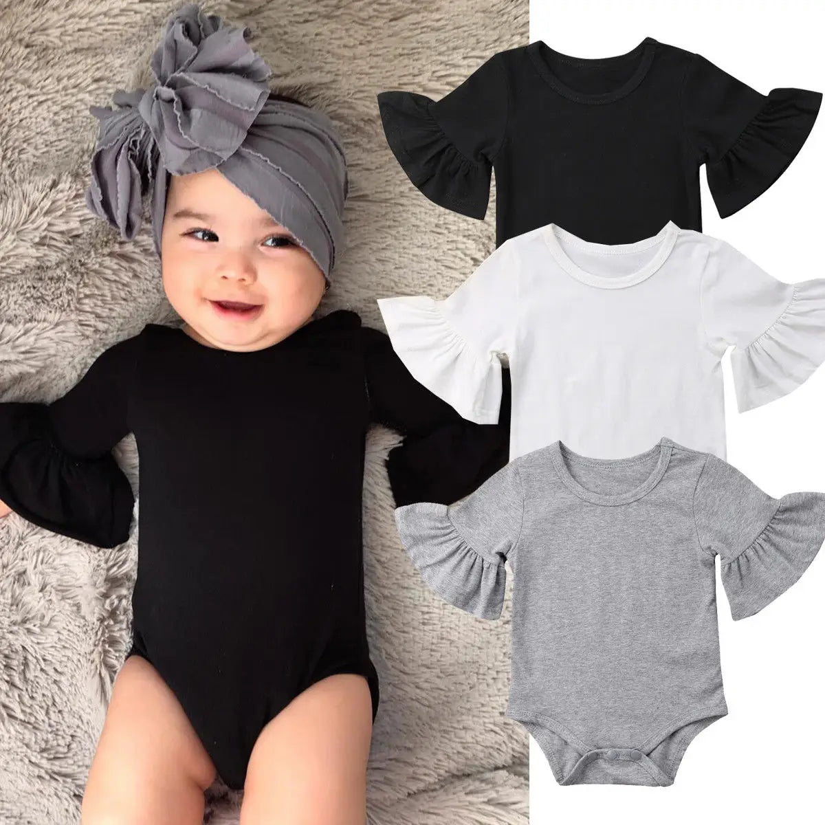Baby in a black onesie with ruffled sleeves and gray headband, surrounded by black, white, and gray onesies.