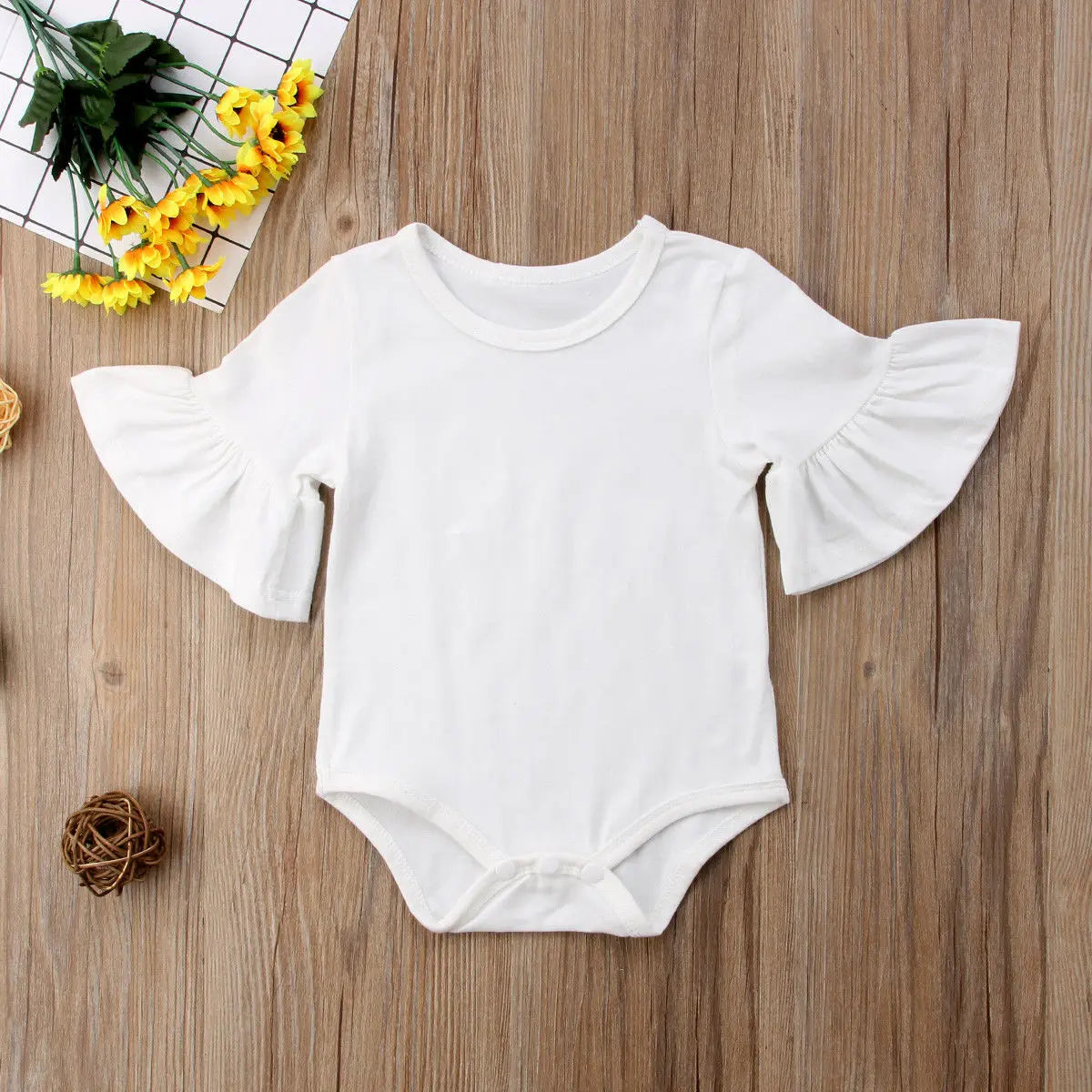 White baby romper with ruffled sleeves on a wooden surface