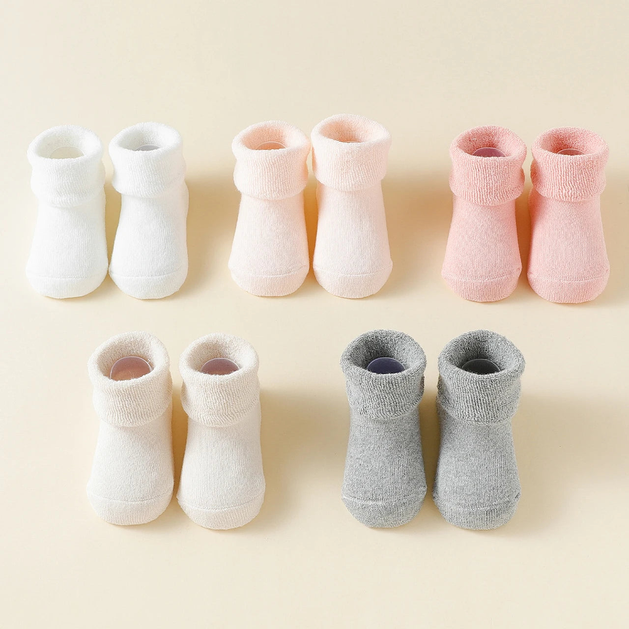 Set of baby booties in white, pink, and gray on a beige background