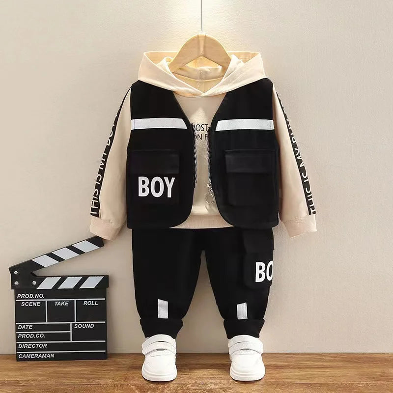 Children's black and beige outfit with 'BOY' text on a wooden floor.