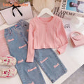 Pink ribbed sweater and blue jeans with pink text on a white surface with magazines and a handbag.