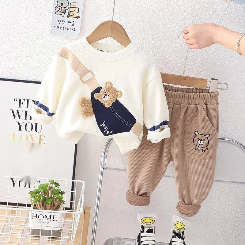 Children's clothing set with white sweater and brown pants on a hanger against a white wall.