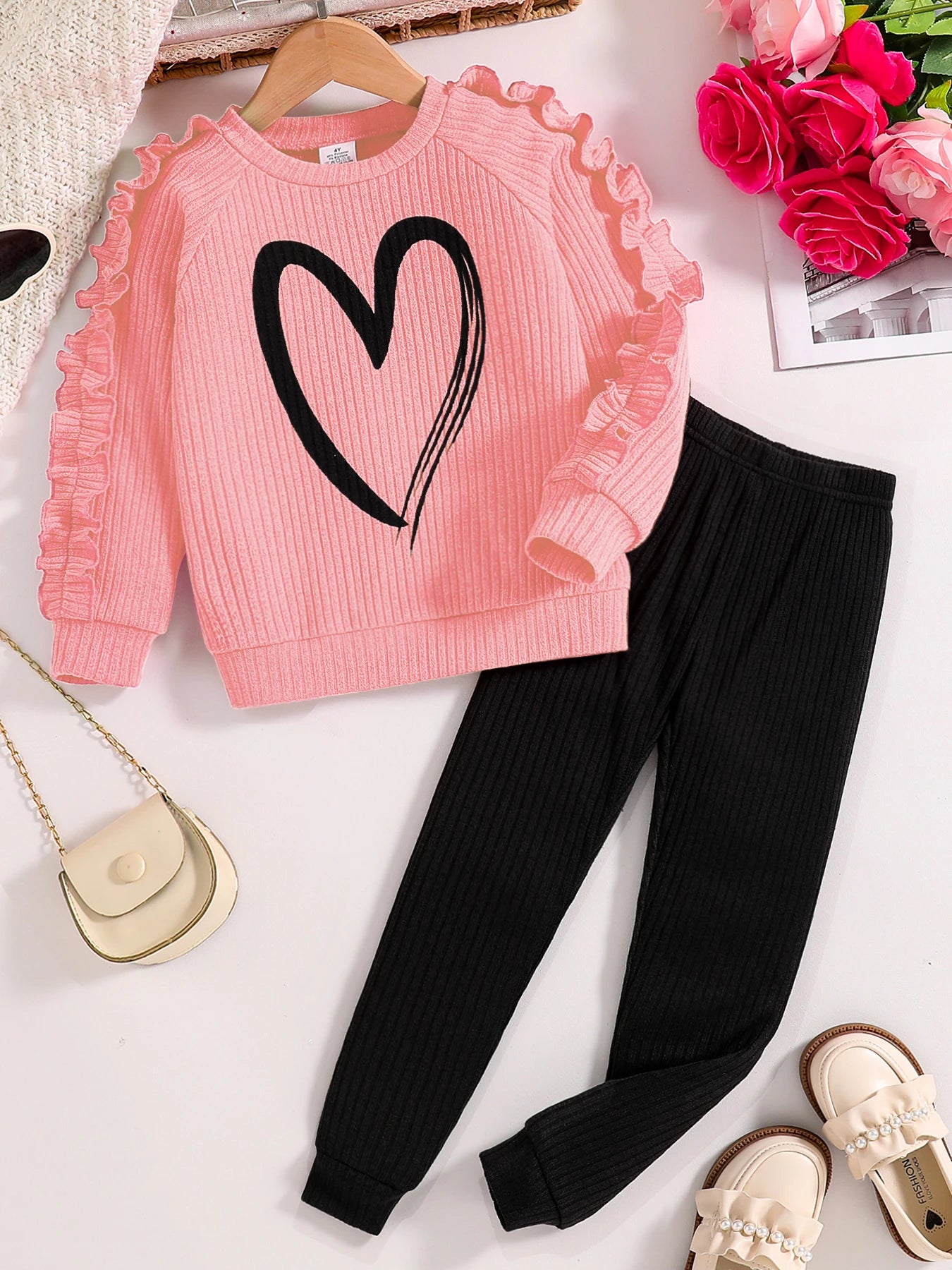 Pink sweater with a black heart design and black pants on a white background