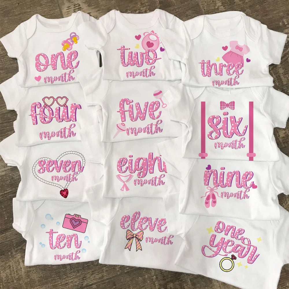 Set of baby onesies with milestone prints on a wooden surface