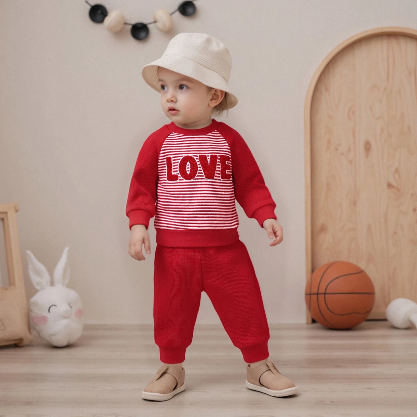 Child wearing a red outfit with 'LOVE' print in a room with toys and a basketball.