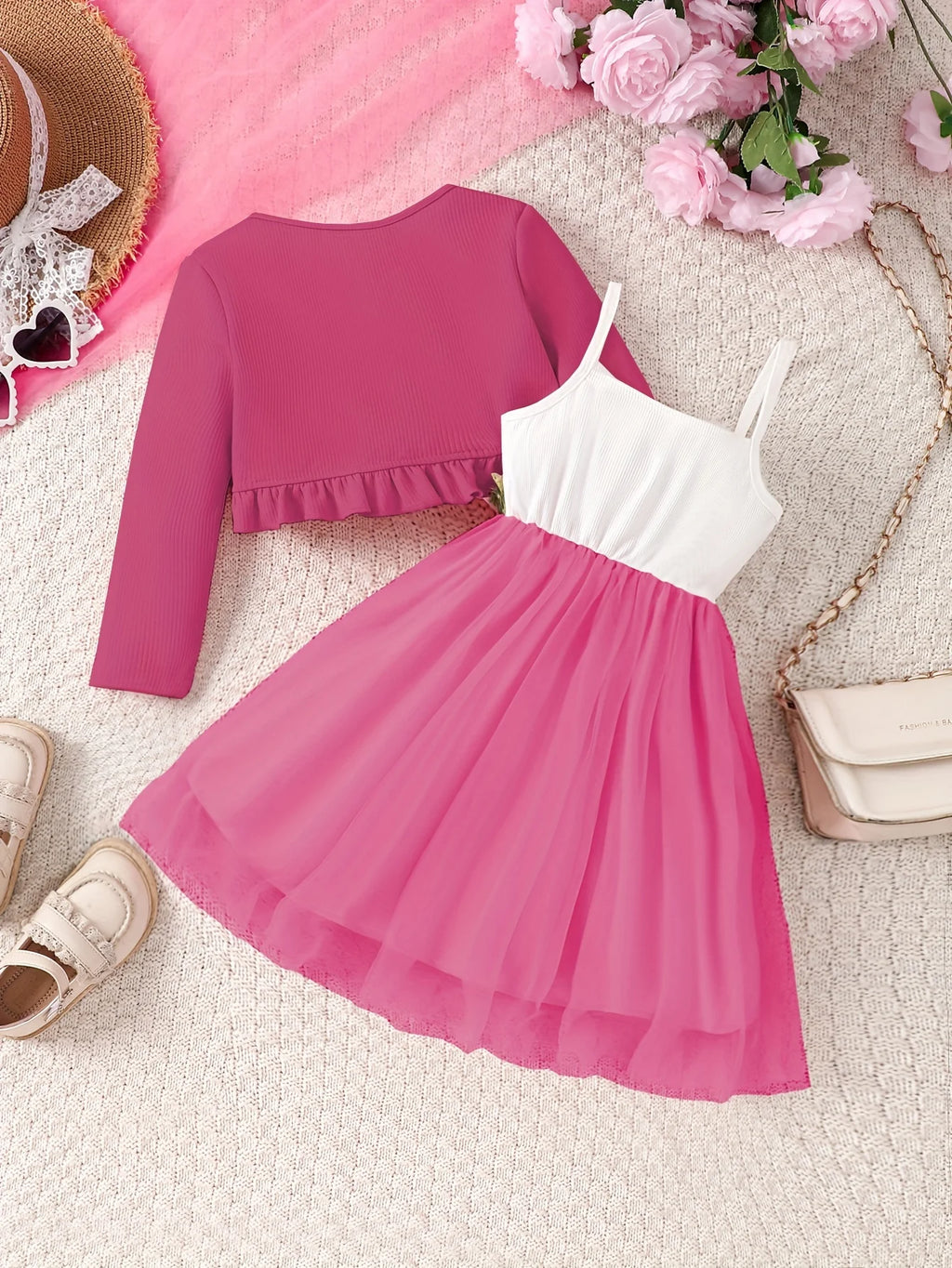 Pink dress with white top and ruffled pink cardigan on a textured surface with flowers and accessories.