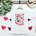 White t-shirt with a dinosaur graphic and 'I Steal Hearts' text on a hanger with decorative elements.