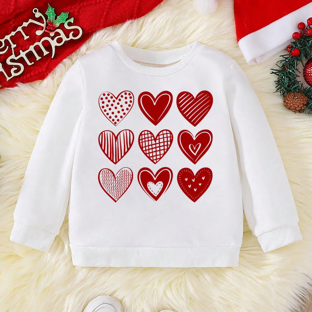White sweater with red heart patterns on a textured surface with Christmas decorations.