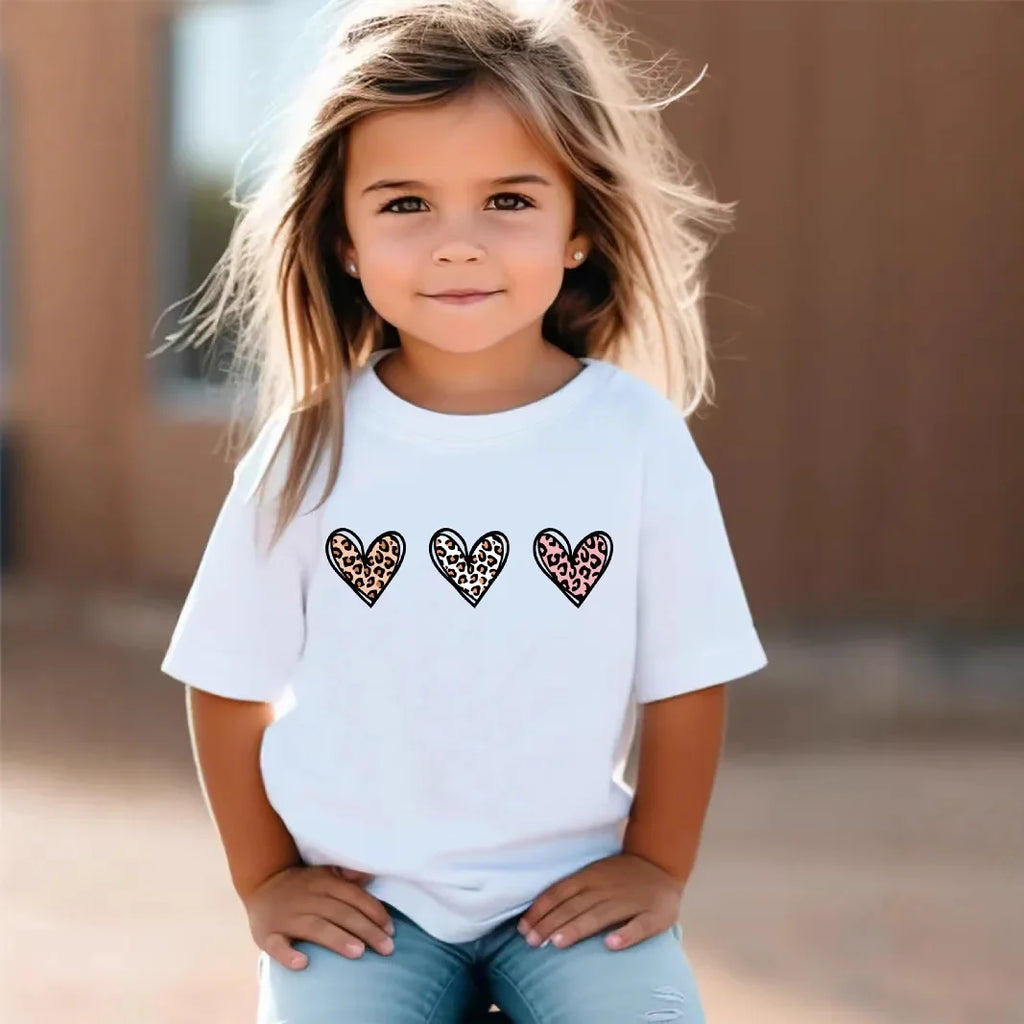 Young girl wearing a white t-shirt with leopard print heart designs outdoors.