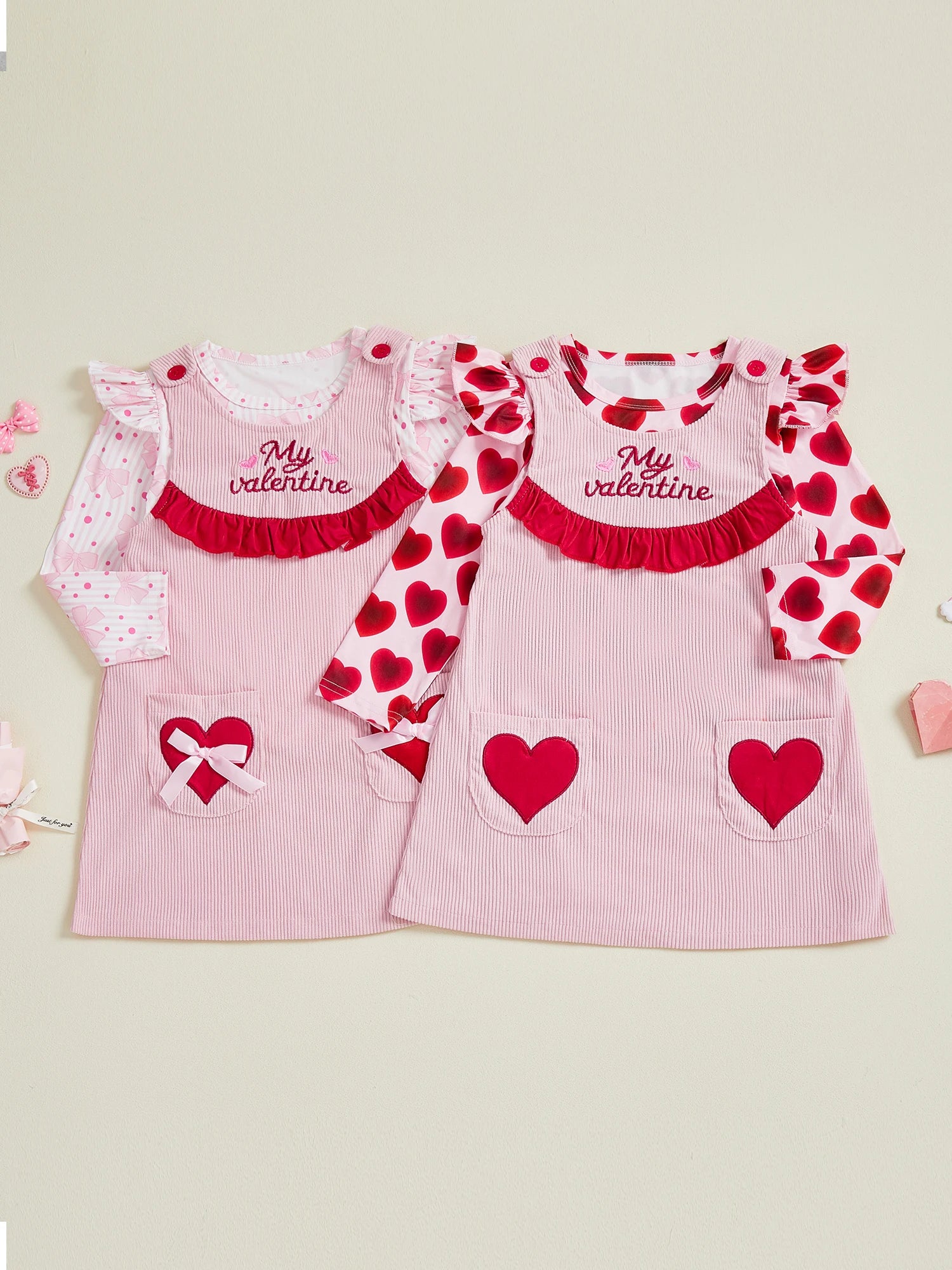 Two pink Valentine's Day dresses with heart designs on a light beige background.