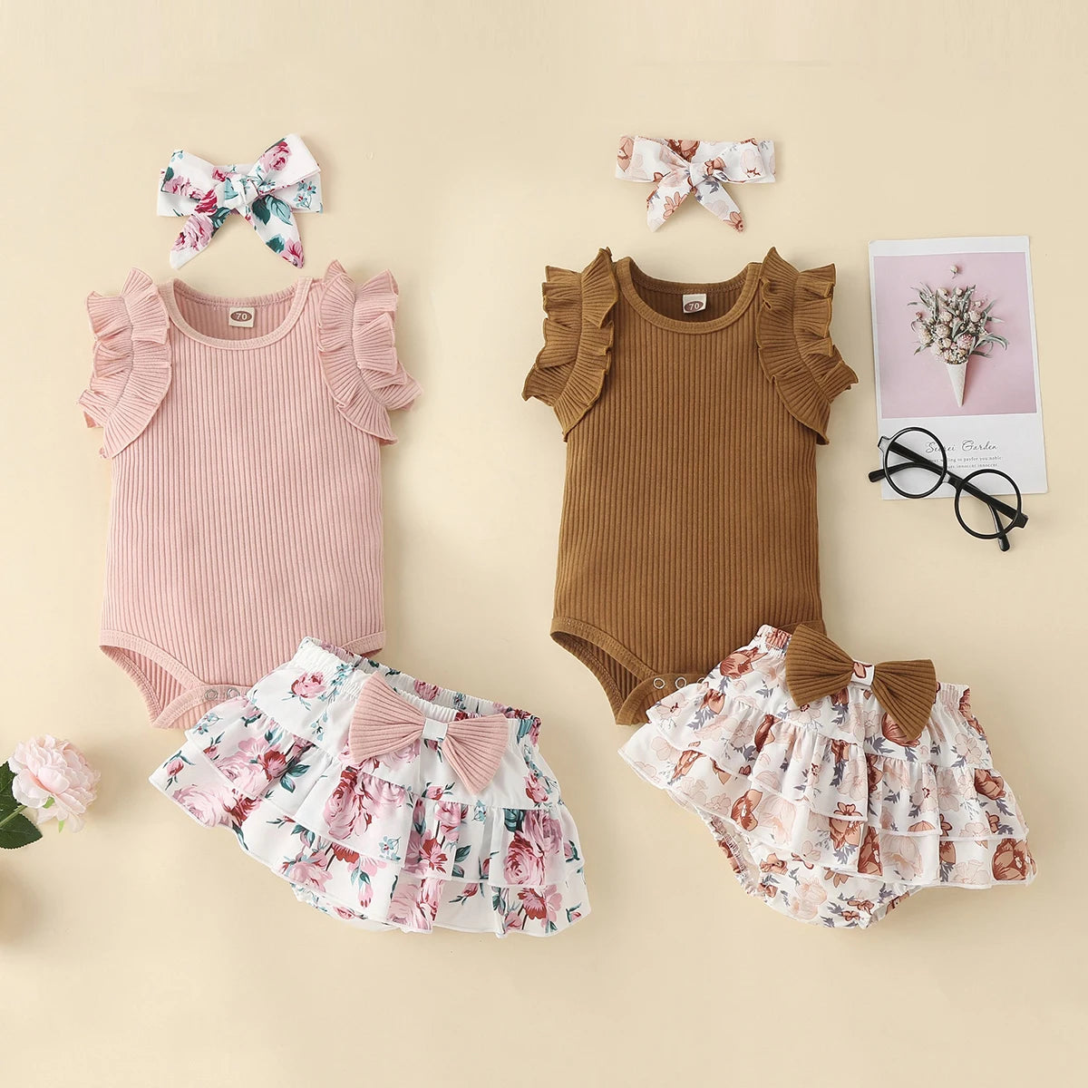 Two baby outfits with ruffled sleeves and floral accessories on a beige background