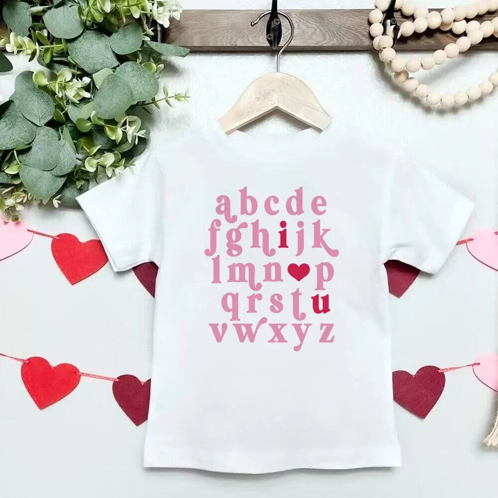 White t-shirt with pink alphabet print on a white background with decorative elements.