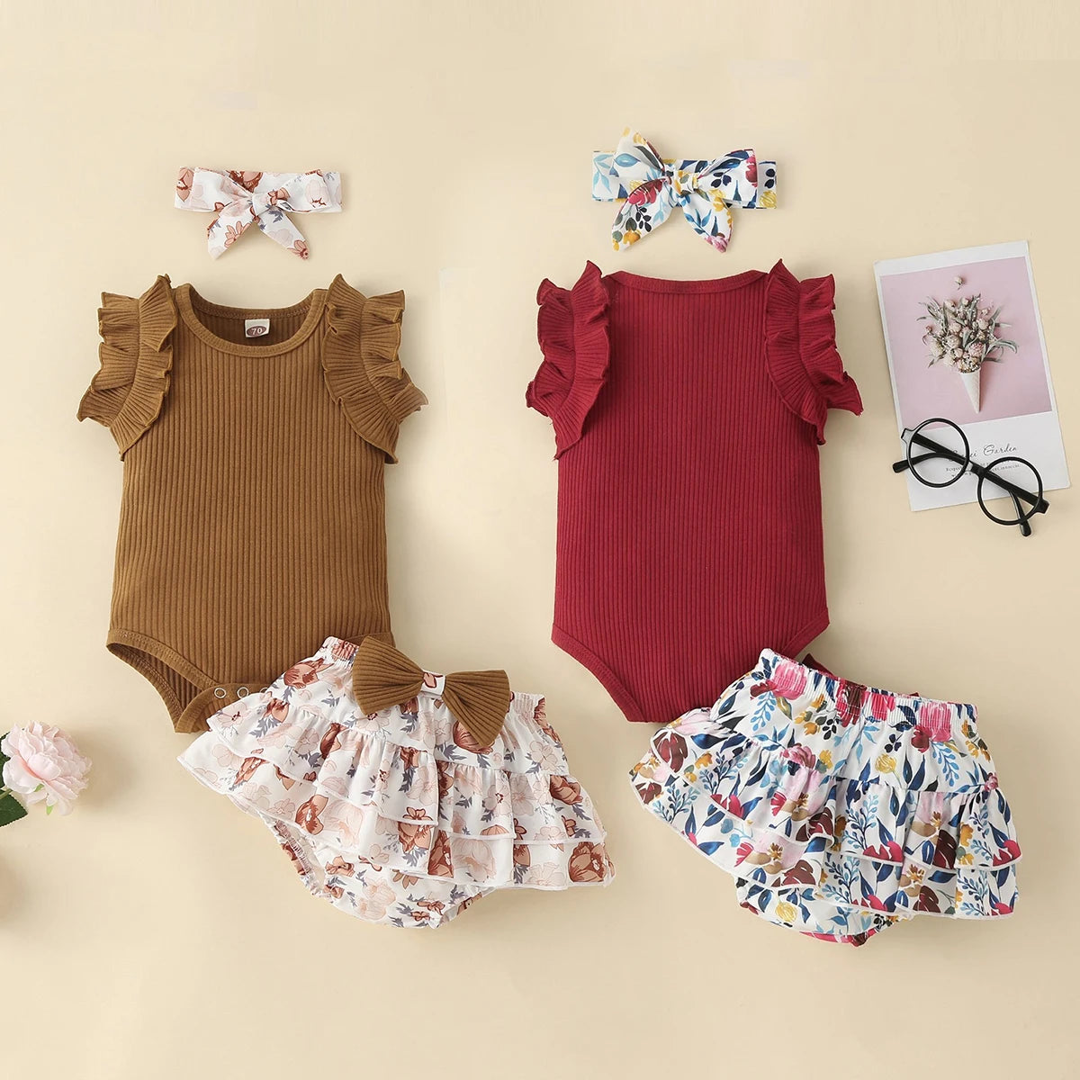 Two baby outfits with ruffled sleeves and floral accents on a beige background.