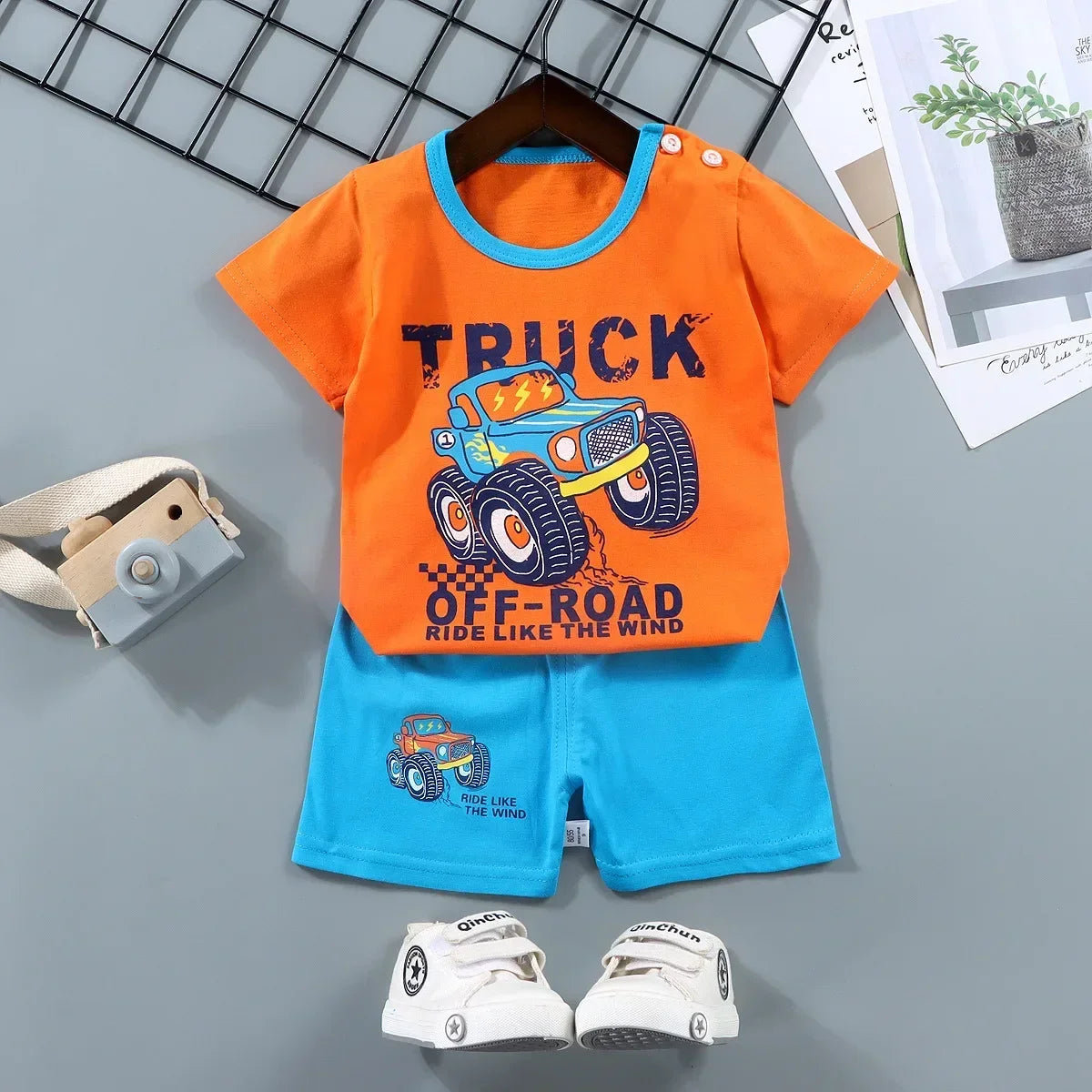 Children's outfit with orange shirt and blue shorts featuring a truck design on a gray background.