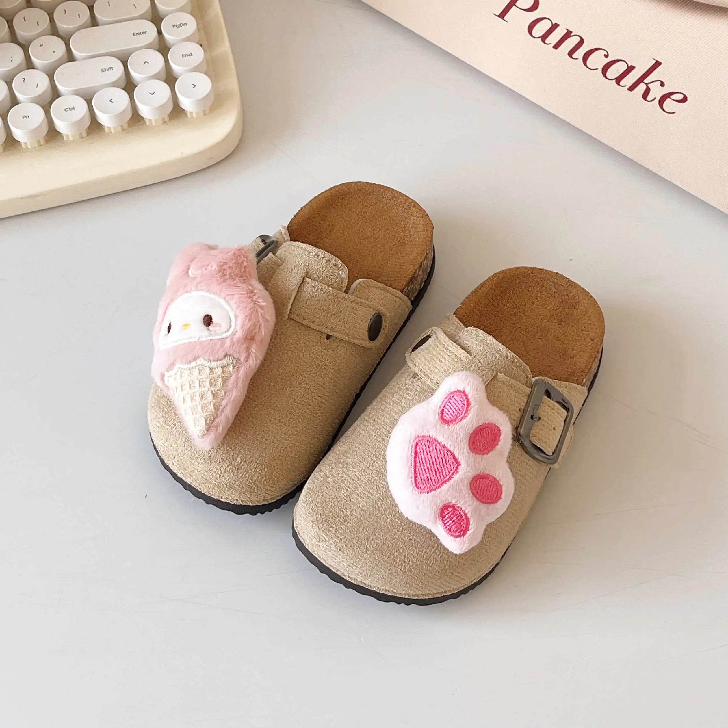 Pair of children's slippers with pink ice cream and paw print design on a light surface.