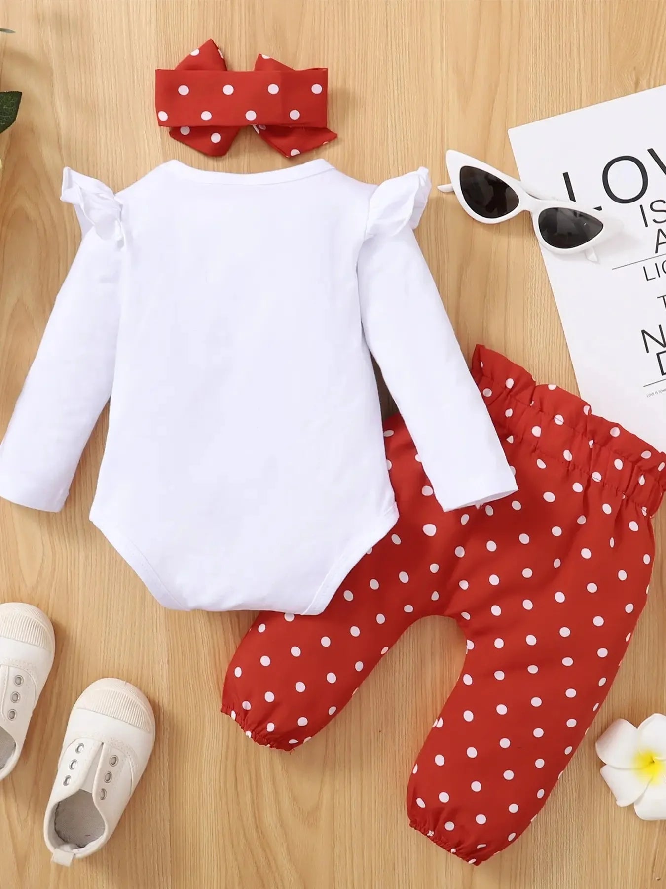 White long-sleeve top and red polka dot pants on a wooden surface with accessories.