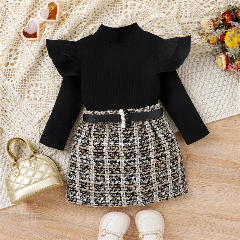 Black ruffled top with a patterned skirt on a wooden surface.
