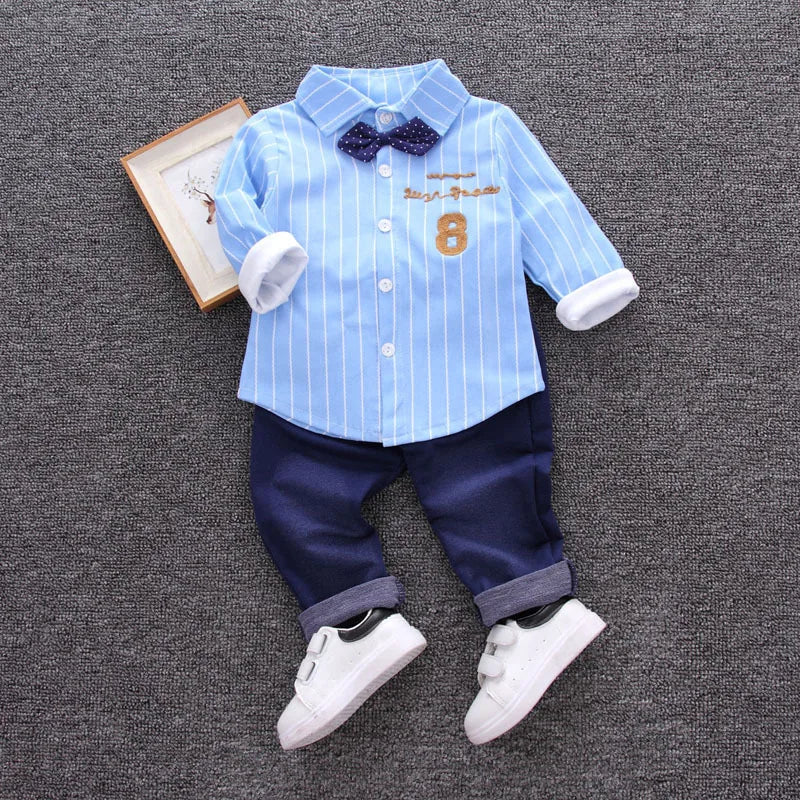 Children's outfit with blue striped shirt, navy pants, and white shoes on a gray background