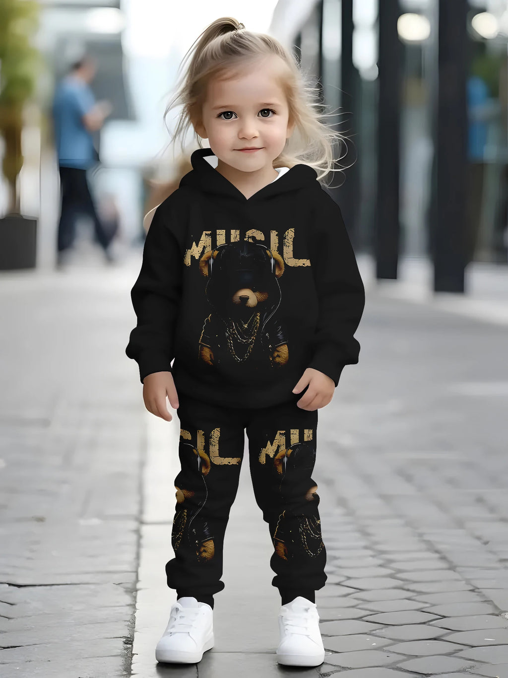 Child wearing a black hoodie and pants with gold text and graphics on a sidewalk.