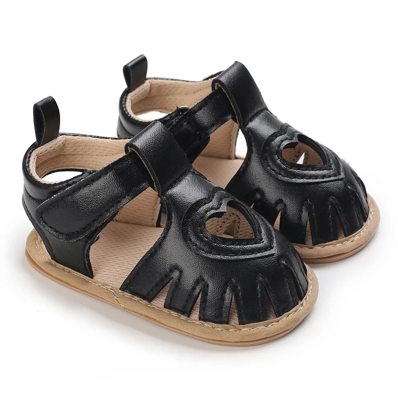 Black baby sandals with brown soles on a white background