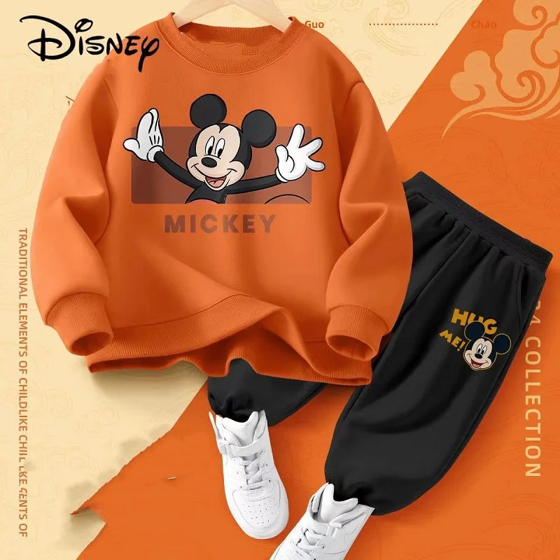 Orange sweatshirt with Mickey Mouse design, black pants, and white sneakers on an orange and beige background with Disney branding.