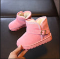 Pink children's snow boots with a buckle held by a hand on a dark surface.