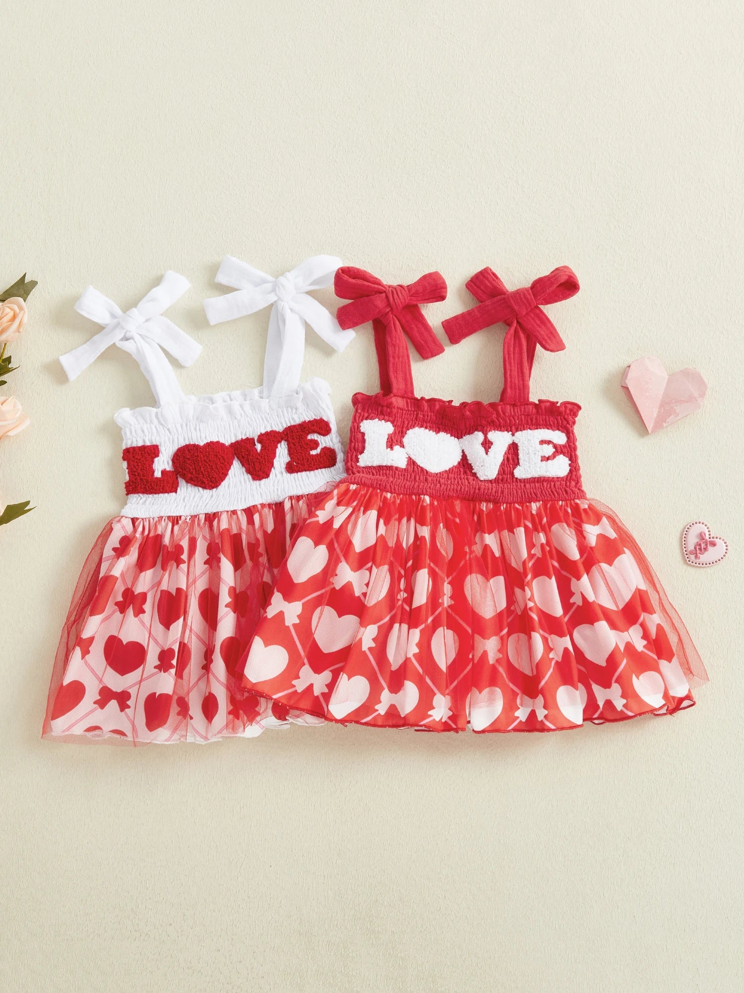Two children's dresses with 'LOVE' text and heart patterns on a beige background.