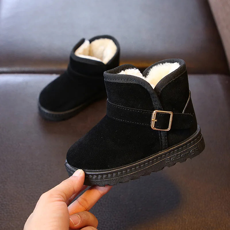 Black children's boots with a buckle held by a hand on a dark surface.