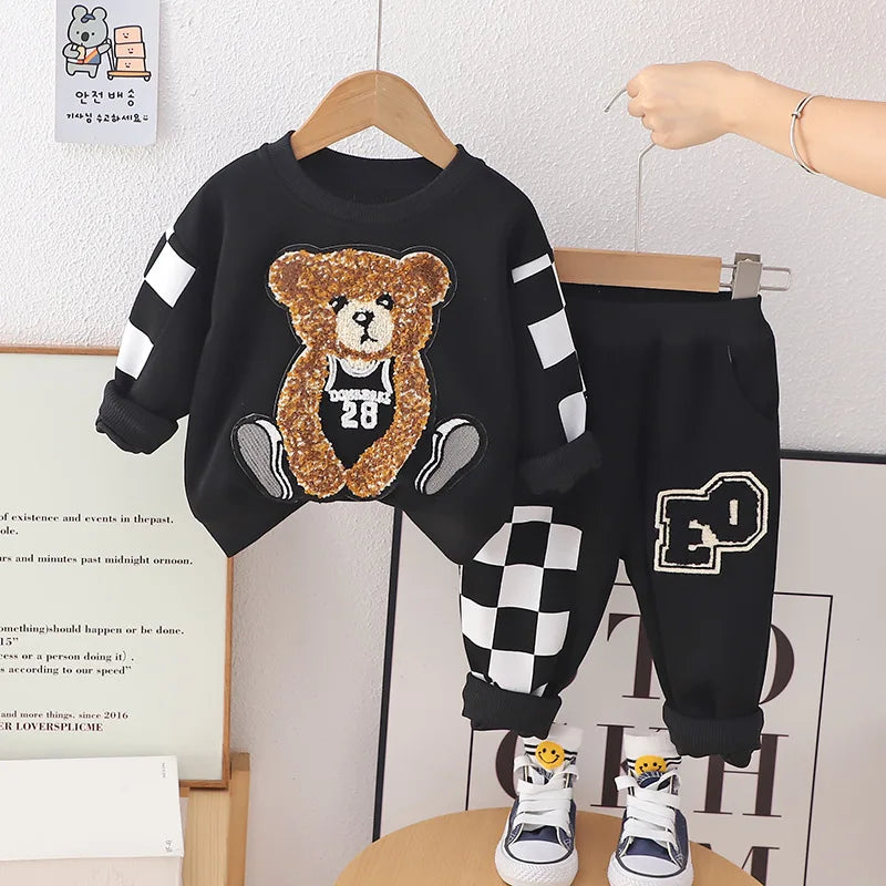 Children's black outfit with teddy bear design on a hanger against a white wall.