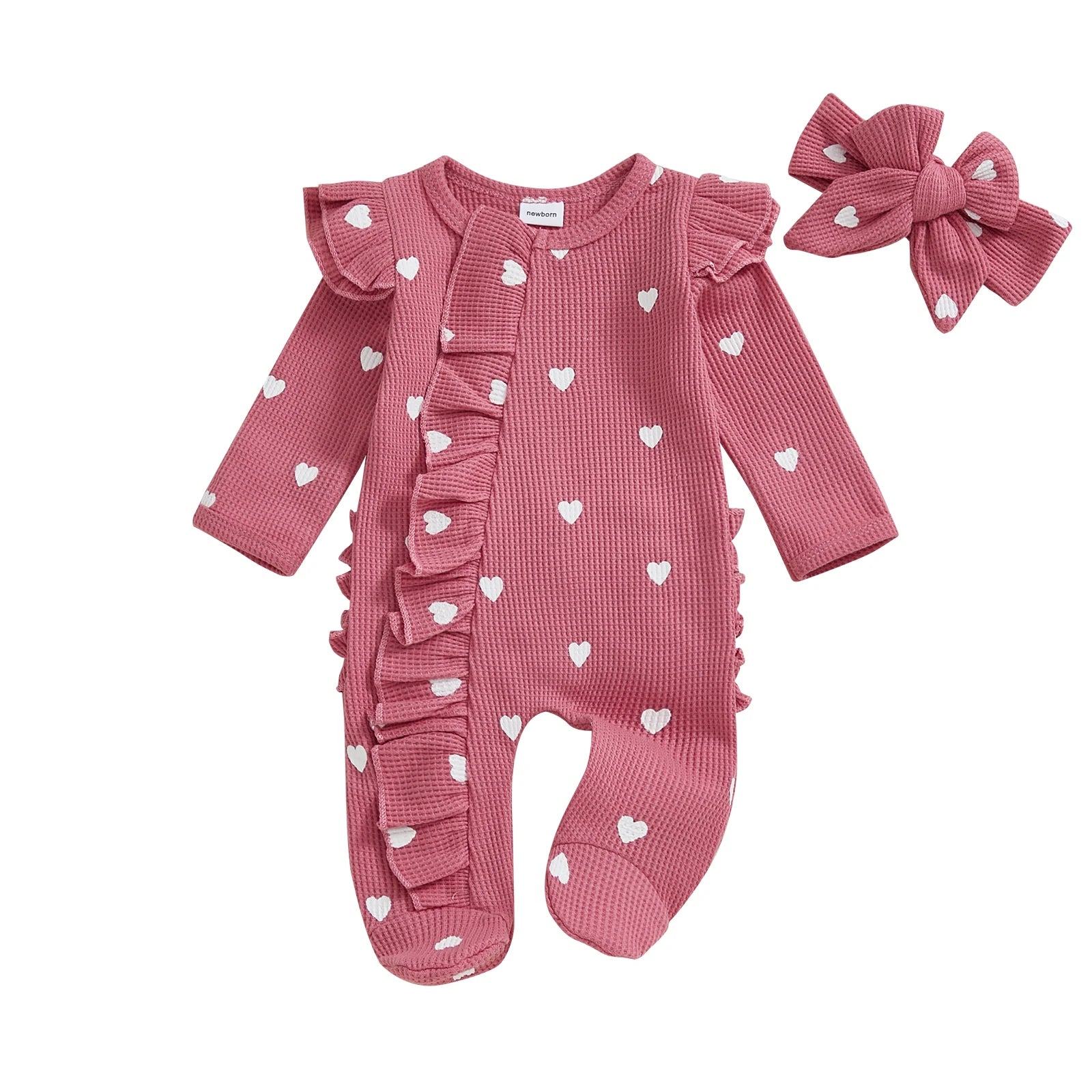 Pink baby romper with ruffles and white heart patterns, accompanied by a matching headband on a white background.