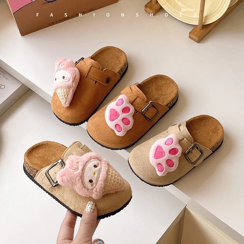 Pair of brown slippers with pink animal-shaped charms on a white surface.