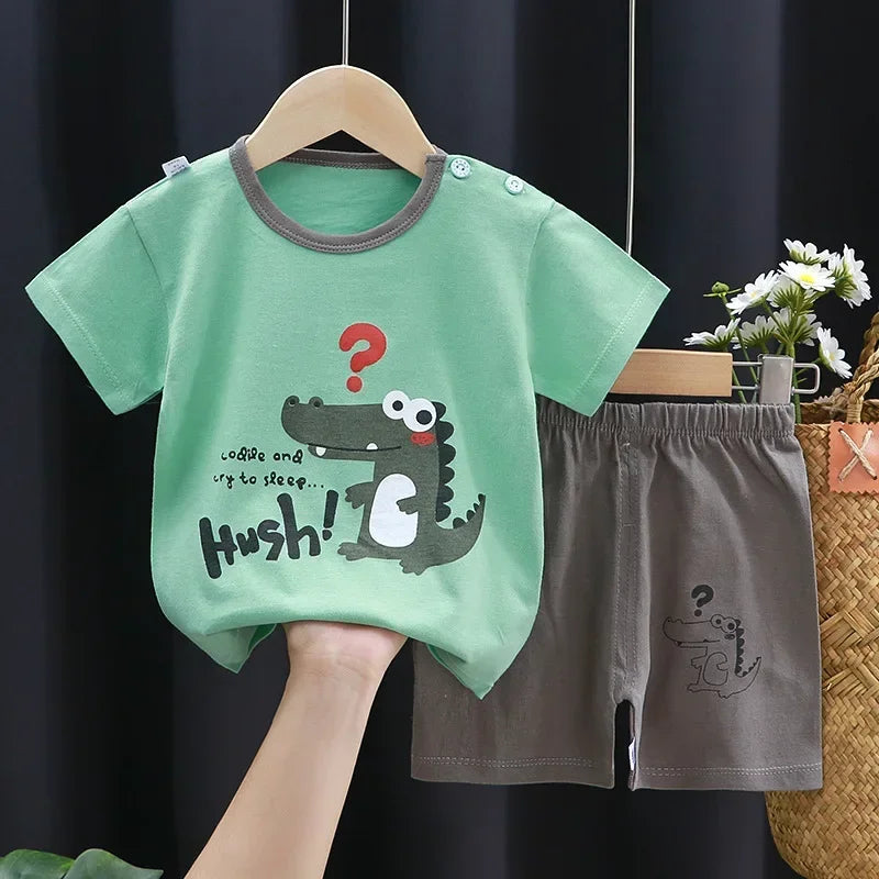 Children's green shirt with crocodile design and gray shorts on a hanger against a dark background.