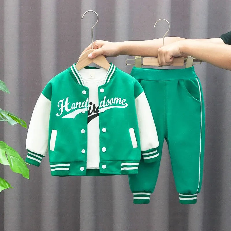 Green varsity jacket and pants set with 'Handsome' text on hangers against a gray curtain background.