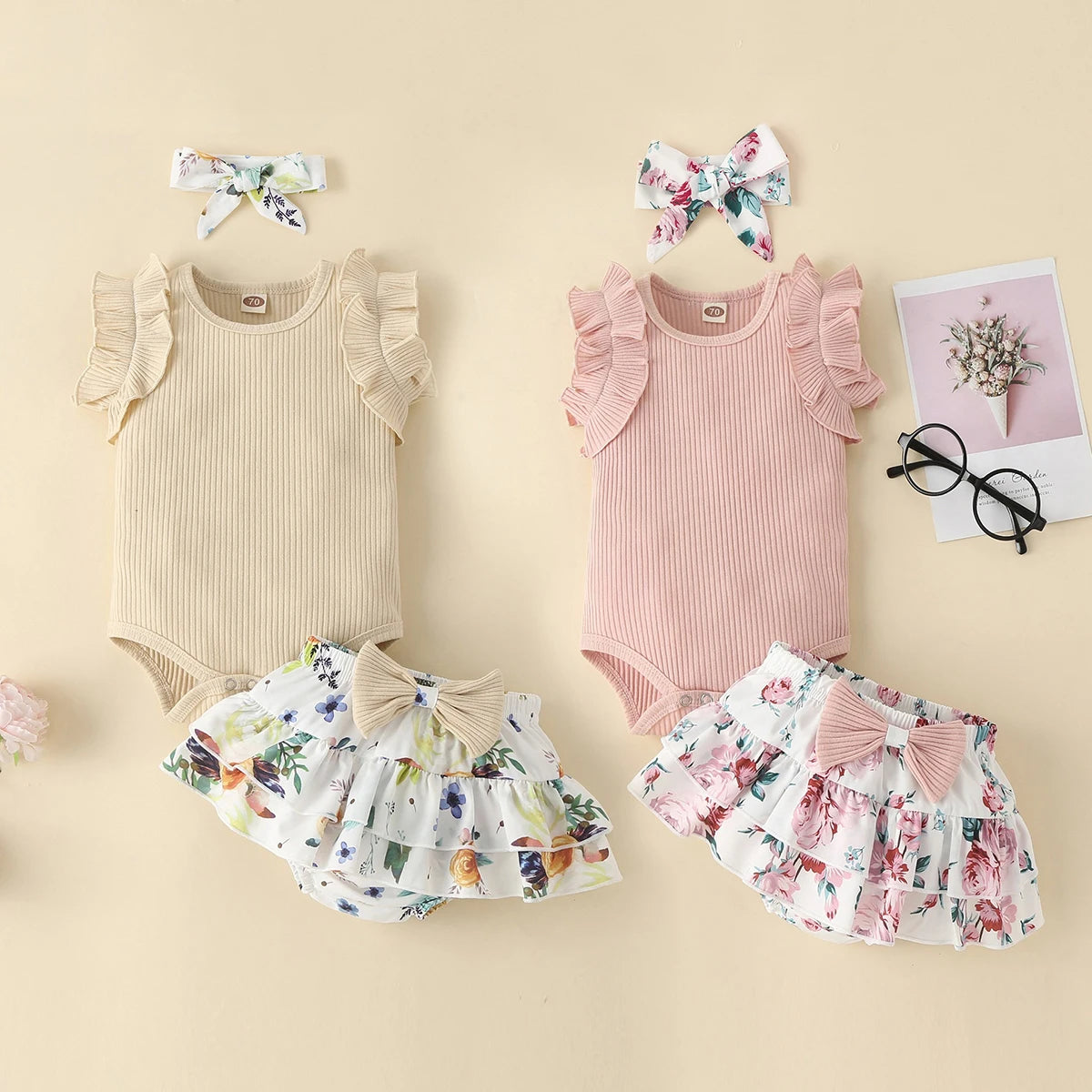 Two baby outfits with floral shorts and headbands on a beige background