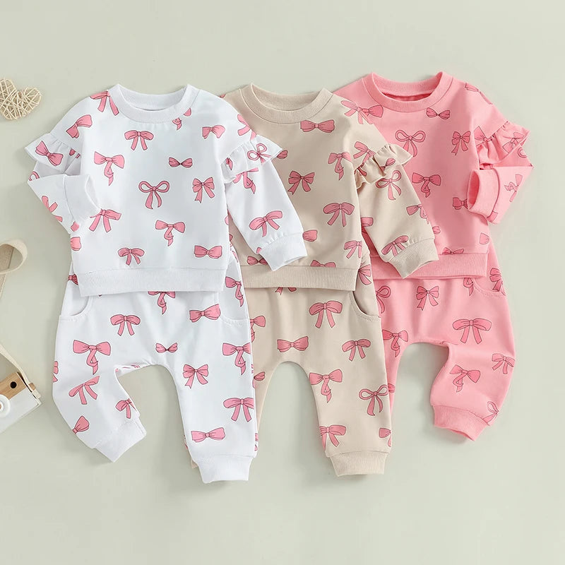 Three sets of baby pajamas with pink bow patterns on a light background