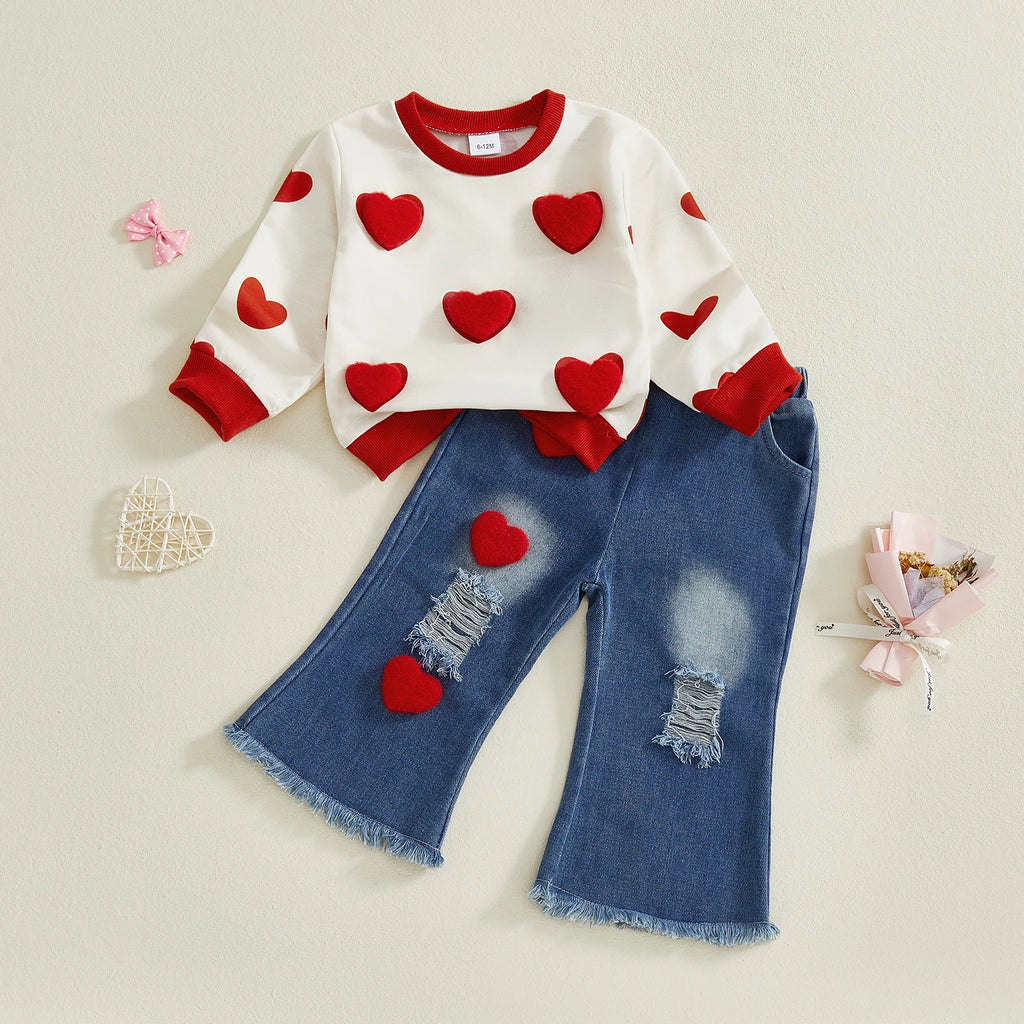 Children's outfit with heart-patterned sweater and distressed jeans on a light beige background