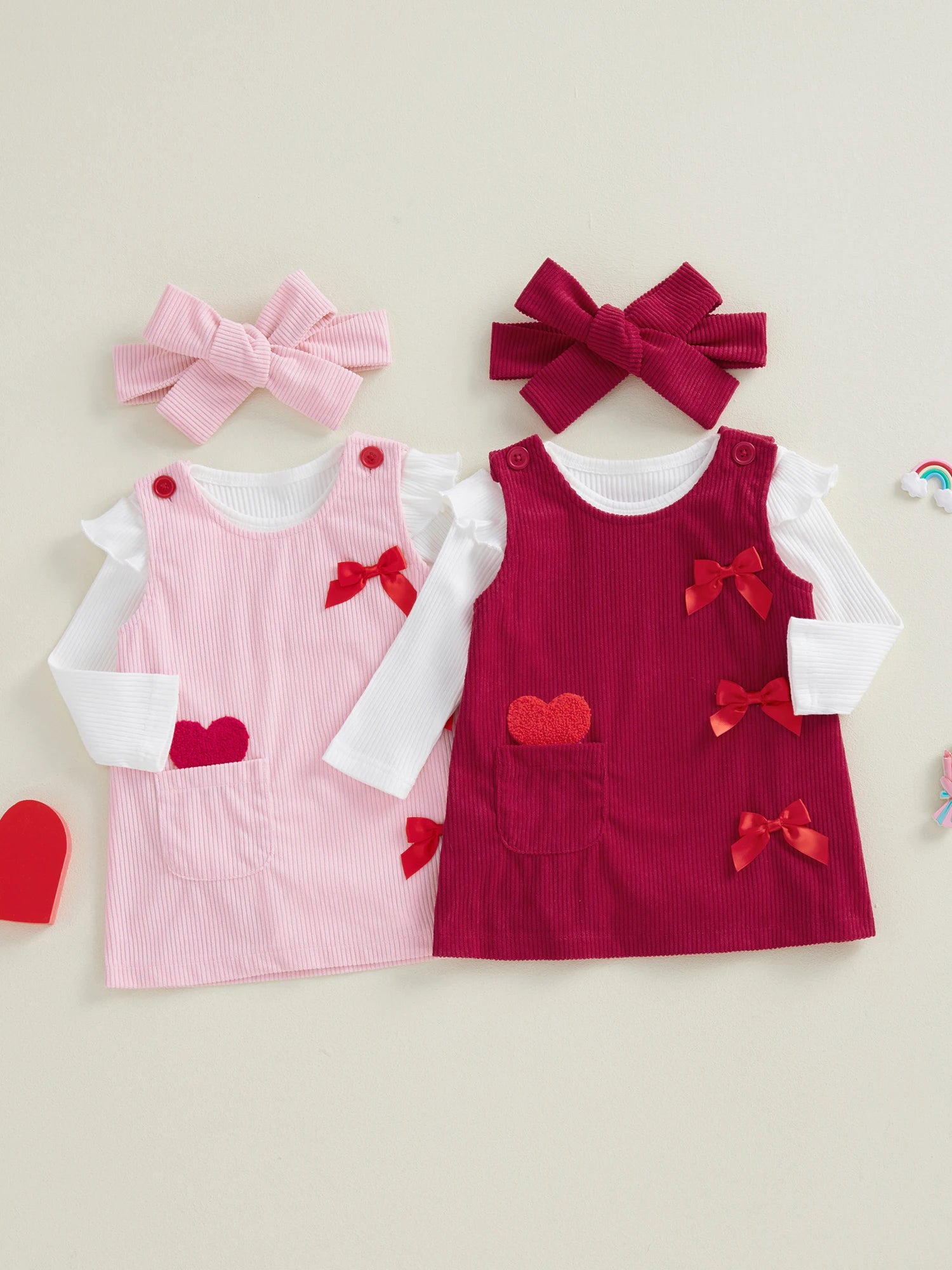 Two children's dresses in pink and red with matching bows on a beige background