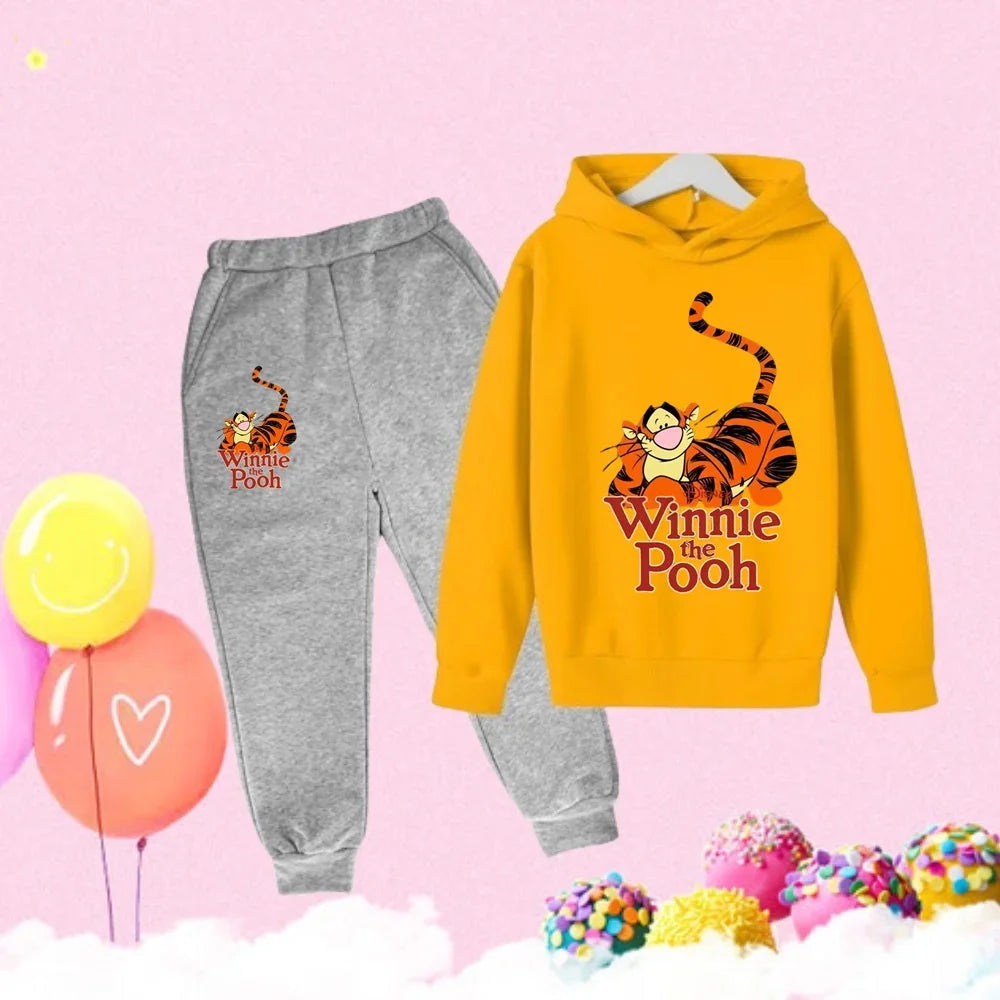 Yellow hoodie and gray sweatpants with 'Winnie the Pooh' design on a pink background with balloons and candy.