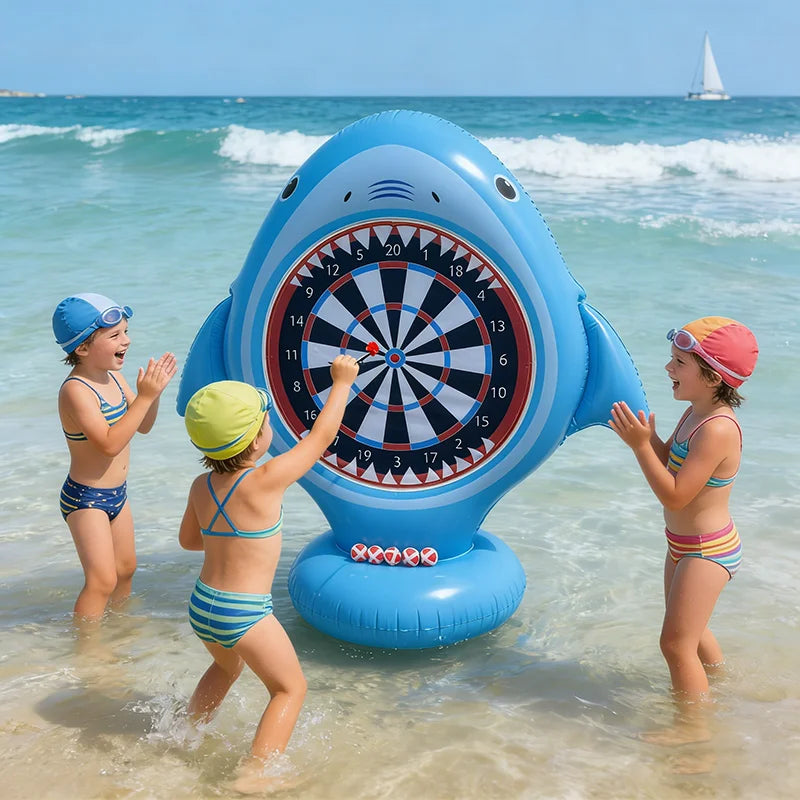 Children playing with a large inflatable shark dartboard in the ocean.