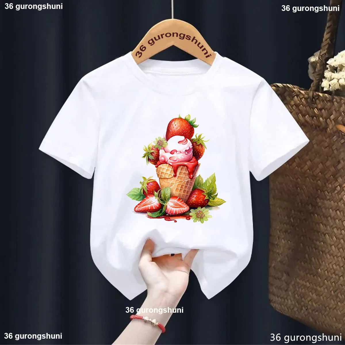 White t-shirt with ice cream cone and strawberry design on a hanger against a dark background.