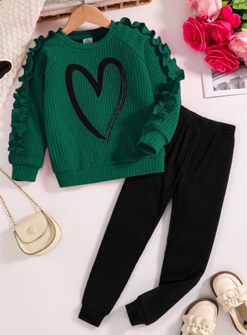 Green sweater with a heart design and black pants on a white surface.