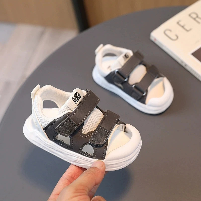 Children's sandals with velcro straps held by a hand on a gray surface.