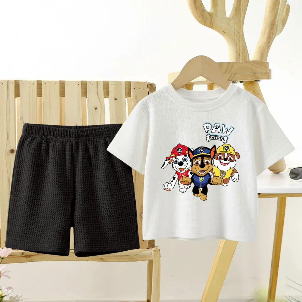 White t-shirt with Paw Patrol design and black shorts on a wooden chair.