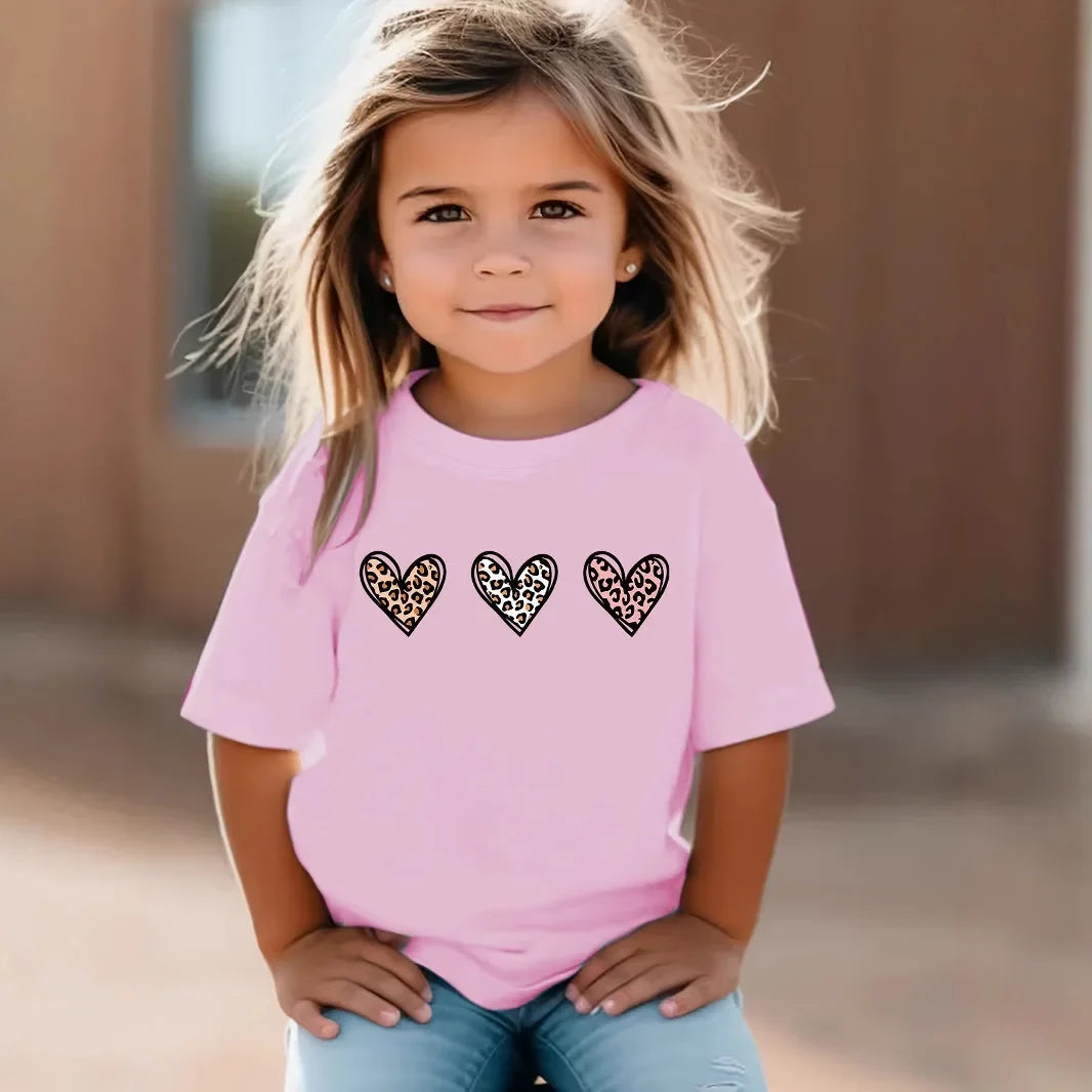 Young girl wearing a pink t-shirt with leopard print hearts outdoors.