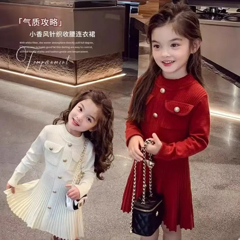 Two young girls in red and white dresses standing in a modern indoor setting.